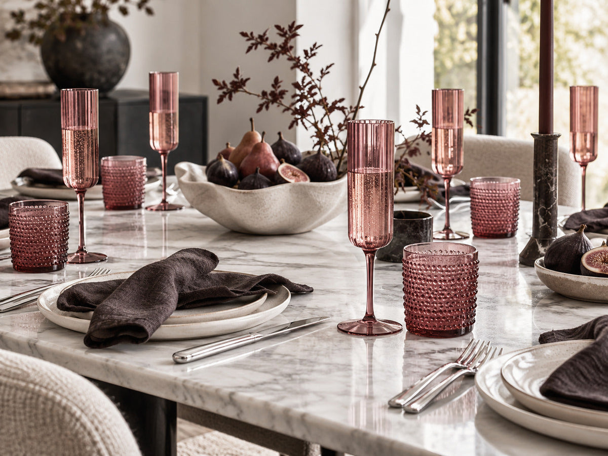 Modern burgundy Thanksgiving tablescape on marble with ribbed champagne flutes, textured tumblers, ivory plates and dark linen