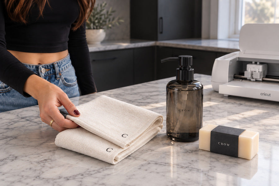 Personalized soap dispenser, ivory guest towels and wrapped soap on a marble counter beside a Cricut.