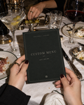 Custom Menu printable party card held above a dinner table with silver flatware